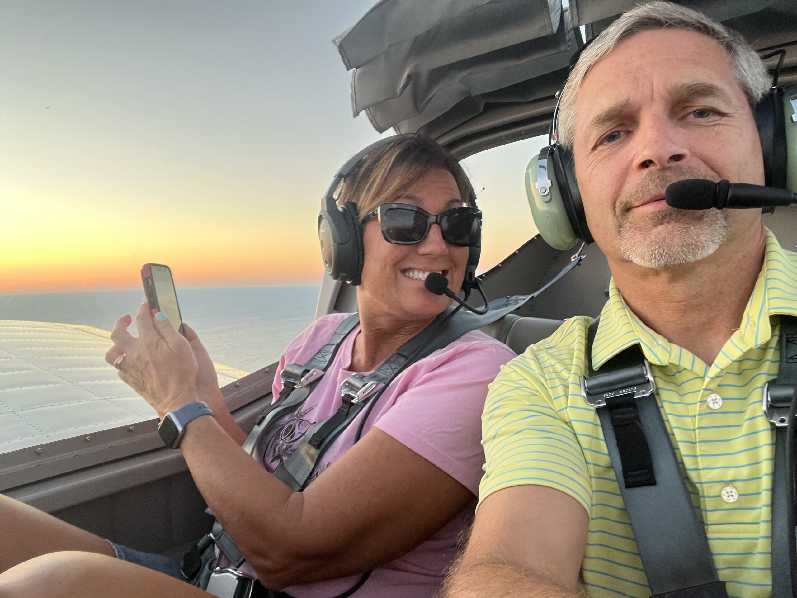 Two passengers wearing headsets during a sunset flight over the shoreline